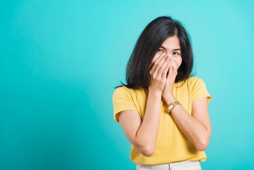 Portrait Asian beautiful happy young woman wears yellow t-shirt she happy excited laughs covering mouth with hands, shoot photo in a studio, on a blue background, with copy space