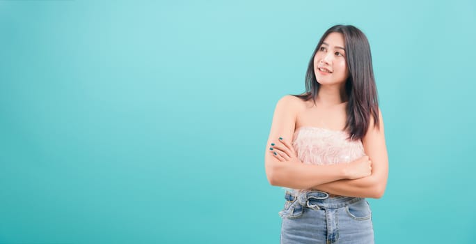 Asian happy portrait beautiful young woman standing smiling white teeth her keeping arms crossed and looking to side on blue background with copy space for text