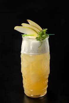 Alcoholic cocktail in a glass cup with a pear on a plain black background