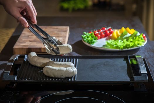 A cook turns over tongs of chicken to a grilled surface