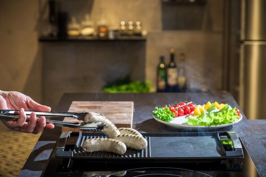 A cook turns over tongs of chicken to a grilled surface