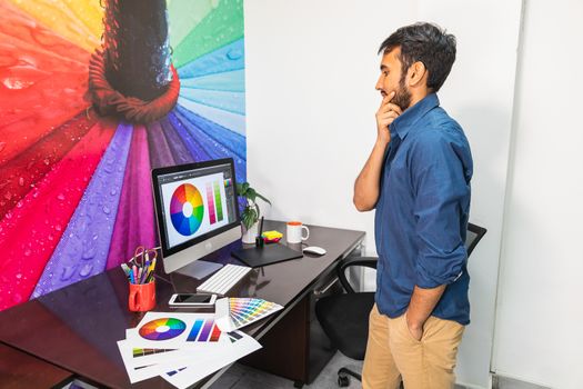 Side view of a young bearded man standing and looking at the computer. Man working in graphics