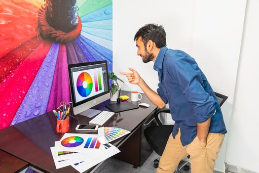 Side view of a young bearded man standing and looking at the computer. Man working in graphics