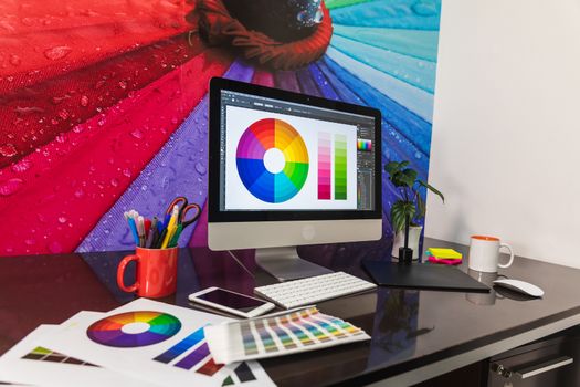 Modern graphic designer office workplace with digital tablet, notepad, colorful pencils, cellphone. Some Color swatch samples over modern desk