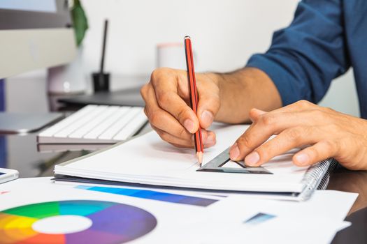 Close up view. Man sitting in office at table. On table color swatch and stationery. Man drawing sketch