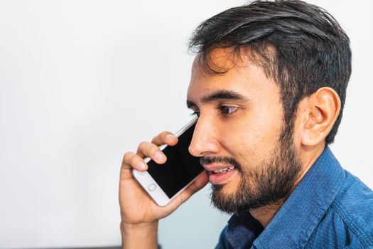 Close up view. Side view. Young bearded businessman in denim shirt using his smartphone.