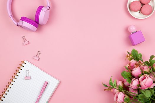 Modern female working space, top view. Women's or girls things, wireless headphones, roses, perfume, stationery on pink backround, copy space, flat lay. Work from home concept. For blog. Horizontal.