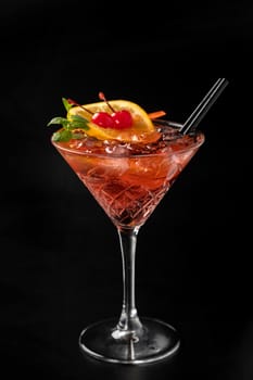 Alcoholic cocktail in a glass with orange on a plain black background