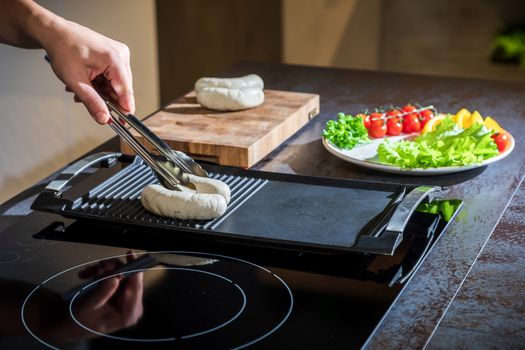 A cook turns over tongs of chicken to a grilled surface