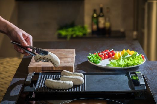 A cook turns over tongs of chicken to a grilled surface