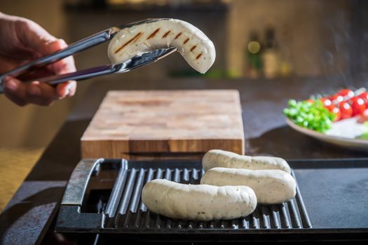 A cook turns over tongs of chicken to a grilled surface