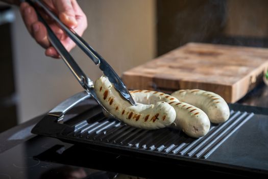 A cook turns over tongs of chicken to a grilled surface