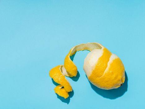 Lemon with spiral peeled zest over blue minimalistic background. Lemon and peel in hard light. Top view or flat lay. Summer minimalistic creative concept and layout. Copy space for text or design.