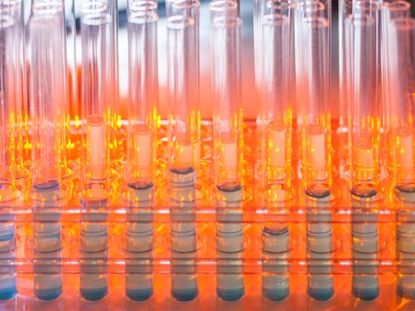 Glass test tubes containing blue liquid on warm orange background. Laboratory, science and research concept.