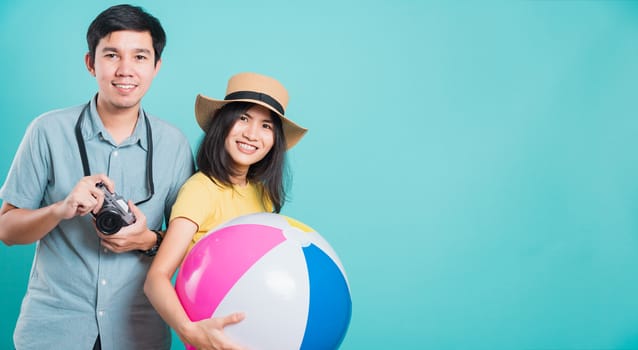 Happy Asian young beautiful woman handsome man couple in summer in holiday travel beach accessories ball and camera isolated on blue background with copy space for text