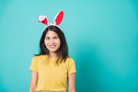 Portrait Asian beautiful happy young woman smile white teeth wear yellow t-shirt standing with bunny ears her looking to camera, on blue background with copy space