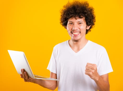 Asian handsome man with curly hair using laptop computer isolate on yellow background with copy space for text