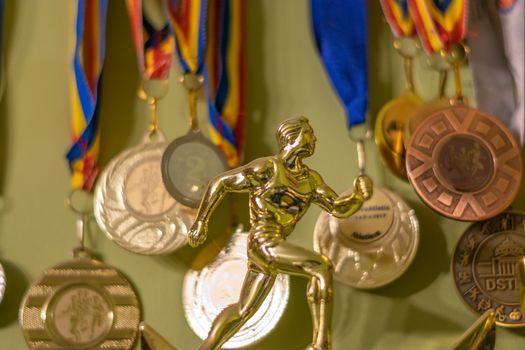 A gold trophy symbolizing an athlete running and many medals in the background, Bucharest, Romania