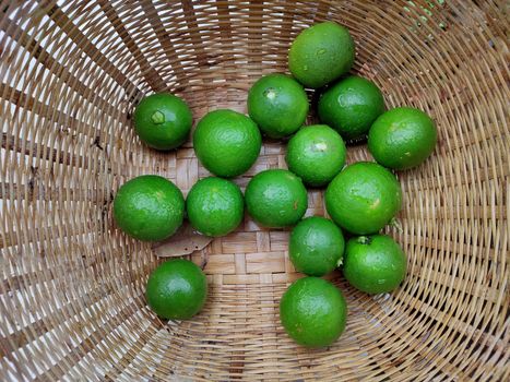 The Fresh green limes in the small colorful baskets on the woven bamboo plate. The Thai traditional fresh market.