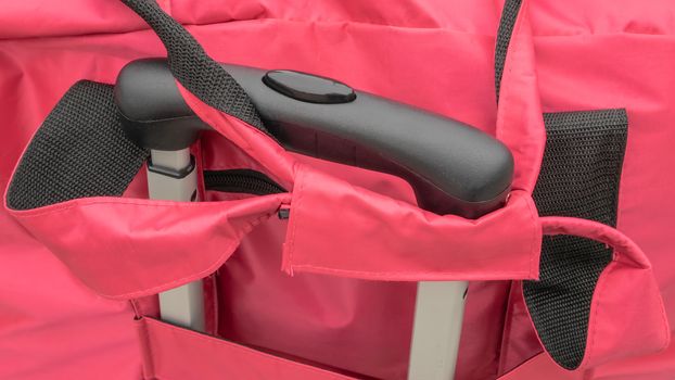 The close up of travel luggage handle with pink travel carry bag.