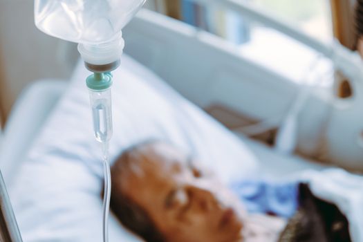 Elderly patients in hospital bed background, Close up of IV saline solution drip