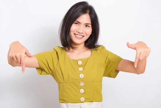 Portrait Asian beautiful young woman standing, She points down to space with fingers and looking to camera, shoot photo in a studio on white background, There was copyspace