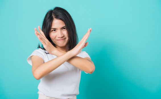 Portrait happy Asian beautiful young woman unhappy or confident standing wear white t-shirt, She holding two crossing arms say no X sign, studio shot on blue background with copy space for text