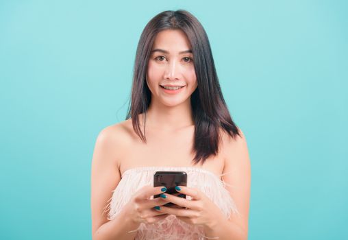 Asian happy portrait beautiful young woman standing smile her  holding smartphone or mobile phone and looking to camera on blue background with copy space for text