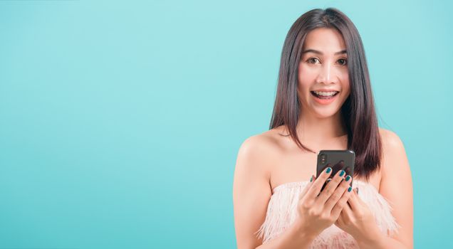 Asian happy portrait beautiful young woman standing smile her  holding smartphone or mobile phone and looking to camera on blue background with copy space for text