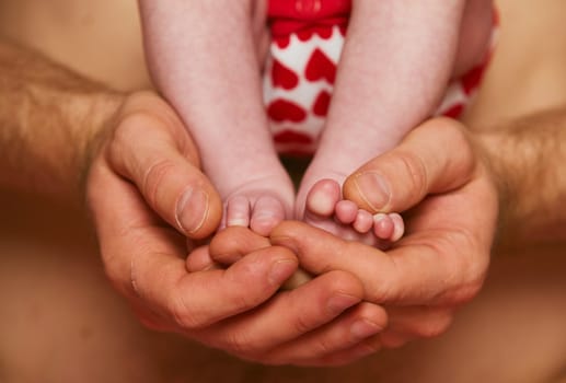 Feet of a newborn baby in the hands of parent. Happy Family concept. Dad hug his baby's legs