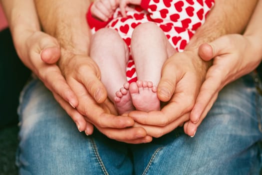 Feet of a newborn baby in the hands of parents. Happy Family concept. Mum and Dad hug their baby's legs