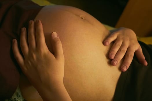 Woman's naked belly on bed in bedroom. Emotional loving moment in pregnancy time - 35 weeks. Baby expectation