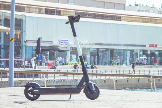 Black electric scooter parking on a deck at Tel Aviv Port commercial district on a summer sunny day. Close up selective focus with copy space.