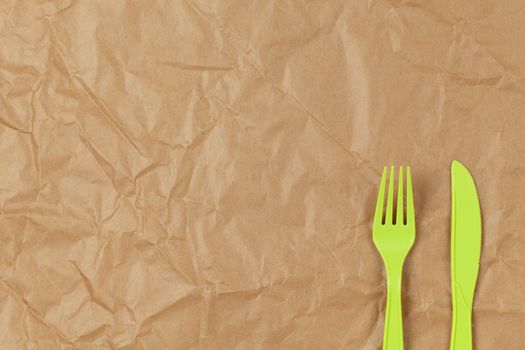 Reusable recyclable green fork, knife made from corn starch on brown crumpled craft paper, copy space. Eco, zero waste, alternative to plastic concept. Flat lay. Horizontal. Close-up.