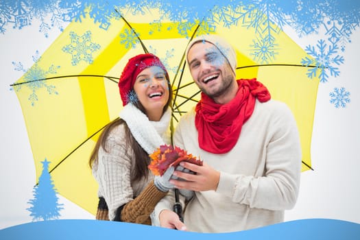 Attractive young couple in warm clothes holding umbrella and leaves against snow flake frame in blue