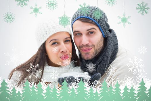 Attractive young couple in warm clothes blowing against snowflakes and fir trees in green