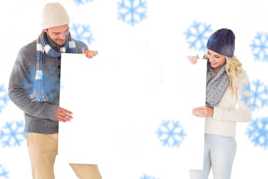 Attractive couple in winter fashion showing poster against snowflakes