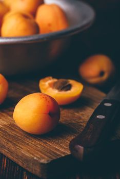 Mellow apricots with knife over old wooden cutting board and metal bowl with fruits