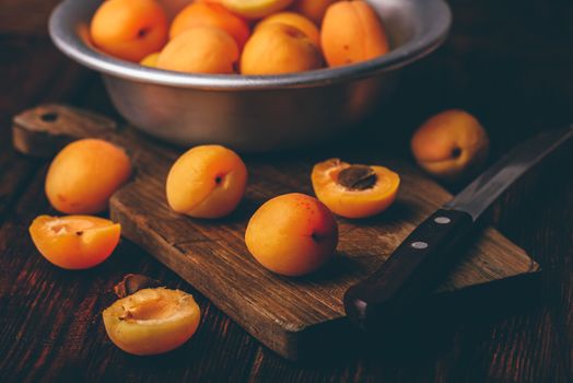 Mellow apricots with knife over old wooden cutting board and metal bowl with fruits