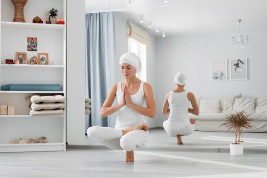 Pretty young woman in sportswear sitting on studio floor in difficult position while doing yoga