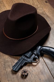 Western wide-brimmed hat and old revolver on a wooden background