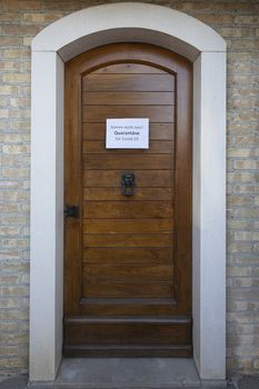 The sign Quarantine  for Covid-19 virus in german language on a wooden entrance door