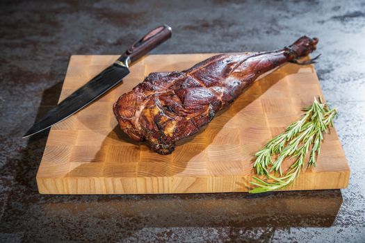 Smoked lamb leg on a wooden board with a knife and rosemary