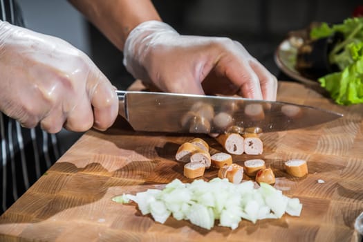 Chef cuts onions and sausages on a wooden cutting board