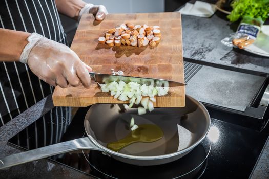 The cook transfers the chopped onion and sausages from the cutting board into a heated frying pan