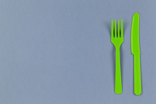 Reusable recyclable green fork, knife made from corn starch on grey background, copy space. Eco, zero waste, alternative to plastic concept. Flat lay, top view. Horizontal. Close-up.
