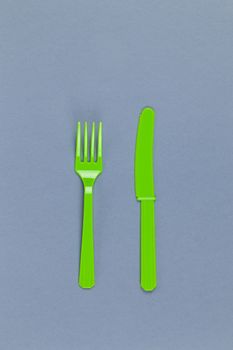 Reusable recyclable green fork, knife made from corn starch on grey background. Eco, zero waste, alternative to plastic concept. Flat lay, top view. Vertical. Close-up.
