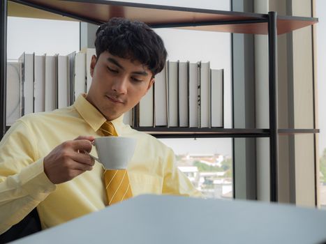A young businessman is relaxing and enjoying the coffee while on the desk during a lunch break.