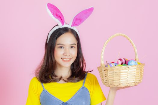 Portrait of a happy young woman wearing Easter bunny ears prepares to celebrate Easter on a pink background.