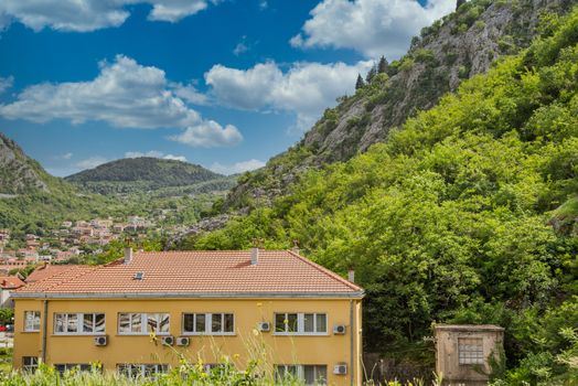 A new plaster apartment building with red tile roof in green mountains of Kotor, Montenegro